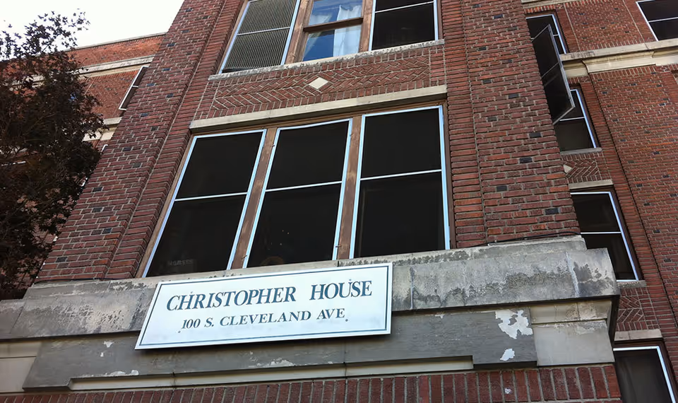 Exterior view of a brick building with a sign that reads 'Christopher House 100 S. Cleveland Ave.' mounted above a concrete ledge below several windows.