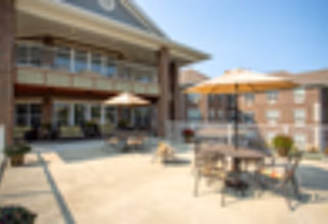 Outdoor patio area at Magnolia Springs Florence with tables, chairs, and umbrellas on a sunny day, surrounded by a multi-story brick building.