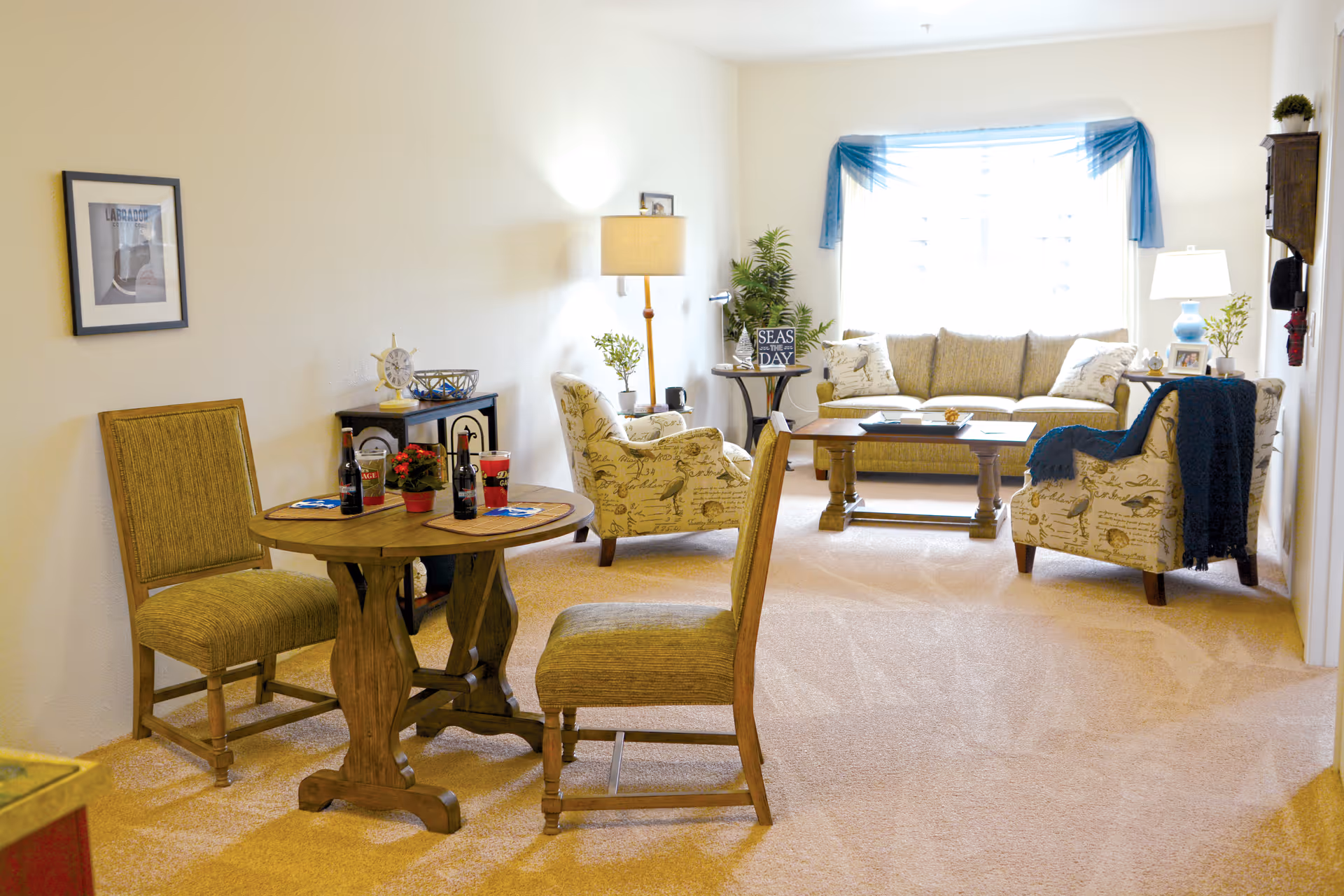 Bright furnished living room with a seating area, coffee table, and a small round dining table with two chairs.