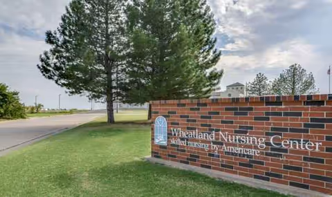 Brick sign reading Wheatland Nursing Center sits beside a grassy lawn and road.