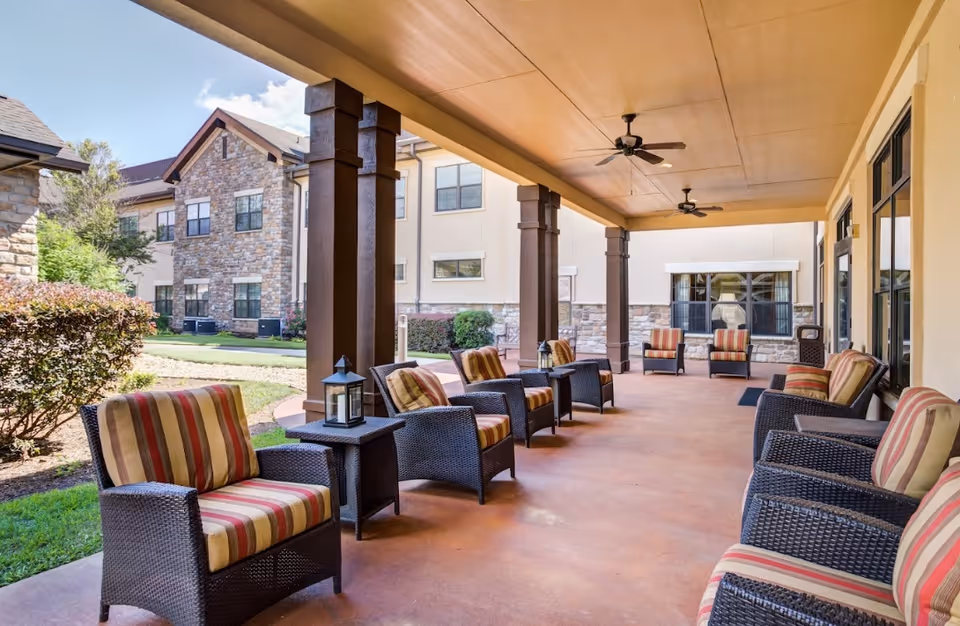 Covered outdoor patio with wicker chairs and striped cushions arranged along columns overlooking a courtyard.