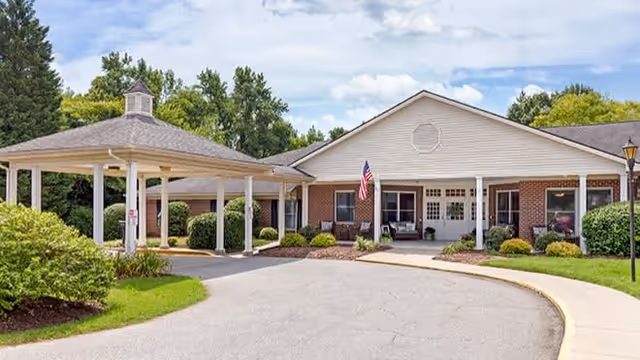 Front exterior of Brookdale High Point senior living facility with a covered porte-cochere, American flag, and landscaped driveway.