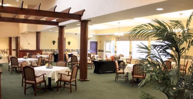 Large dining room with multiple tables and chairs, wooden columns, and potted plants.