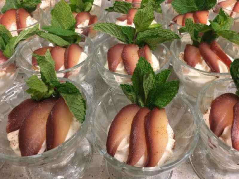 Multiple glass dessert cups filled with a creamy dessert topped with slices of poached pear and fresh mint leaves.