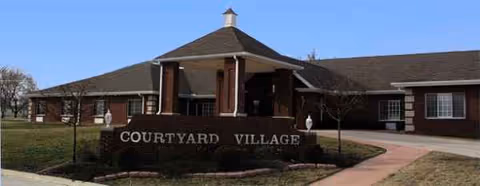 Brick senior living facility entrance with a Courtyard Village sign under a covered portico.