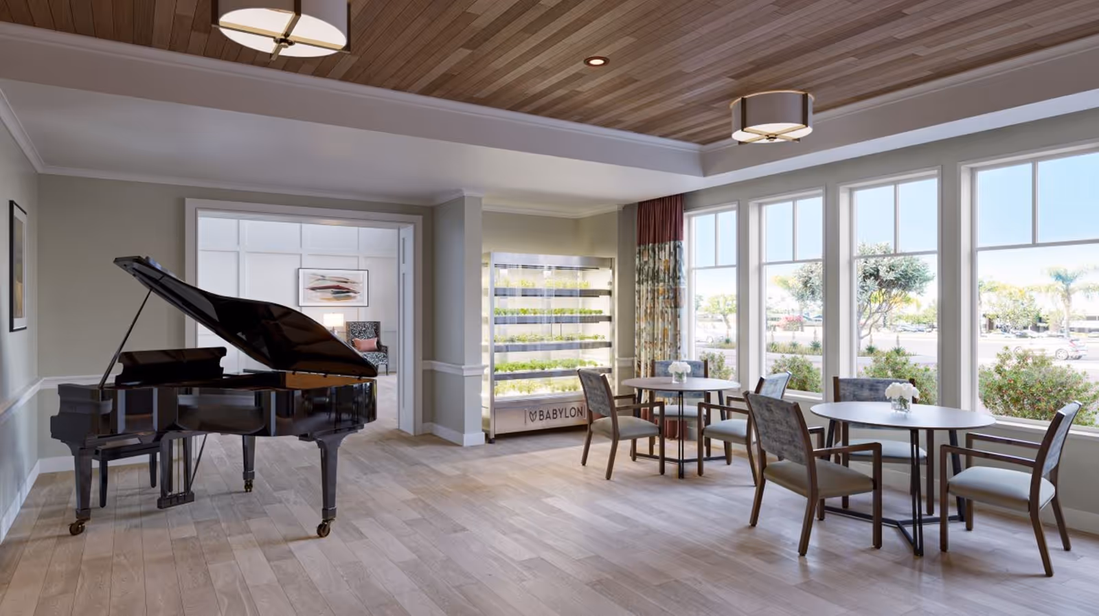 Bright communal living area with a grand piano, round tables and chairs by large windows and a vertical plant display.
