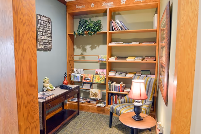 Cozy reading nook with built-in bookshelves, an upholstered chair, side table with a lamp, and a small desk.