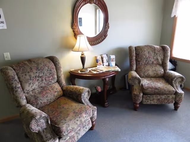 Two floral armchairs sit around a wooden table with lamp in a cozy living room.