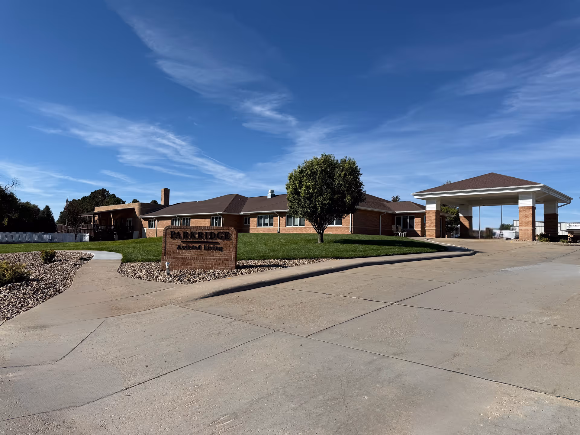 Exterior front view of Park Ridge Assisted Living building with a driveway, entrance canopy, lawn, and a brick sign.