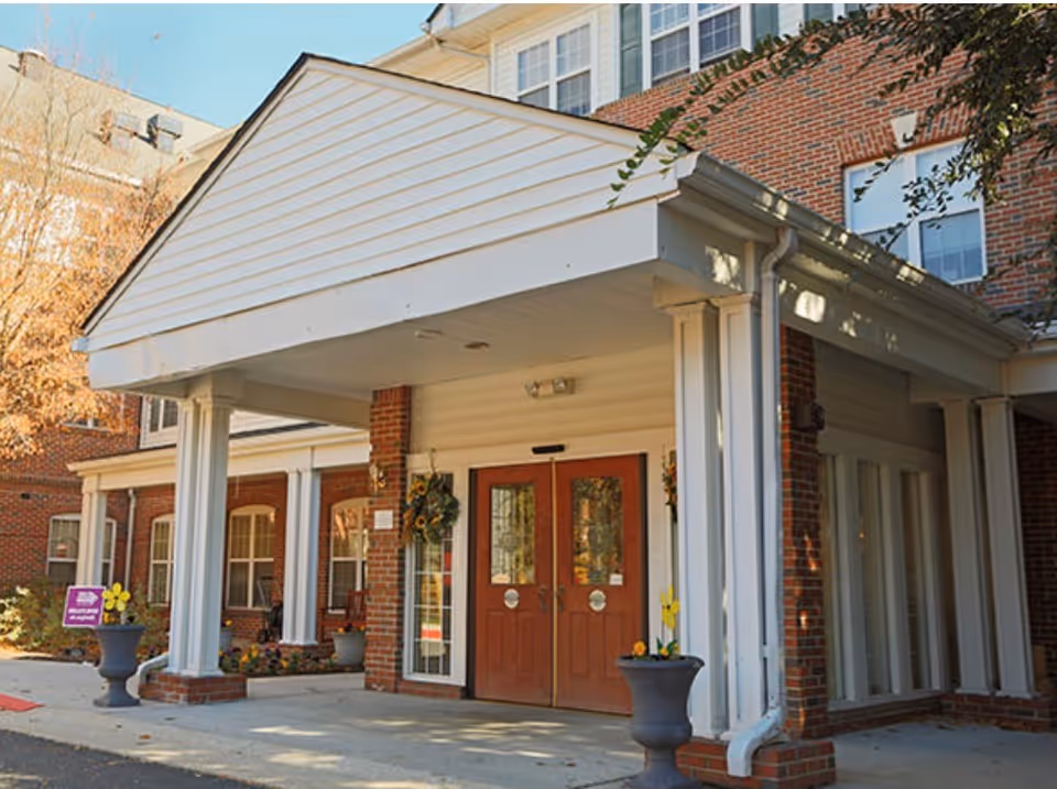 Entrance to Charter Senior Living Towson with brick facade, columns, double red doors, and potted plants.