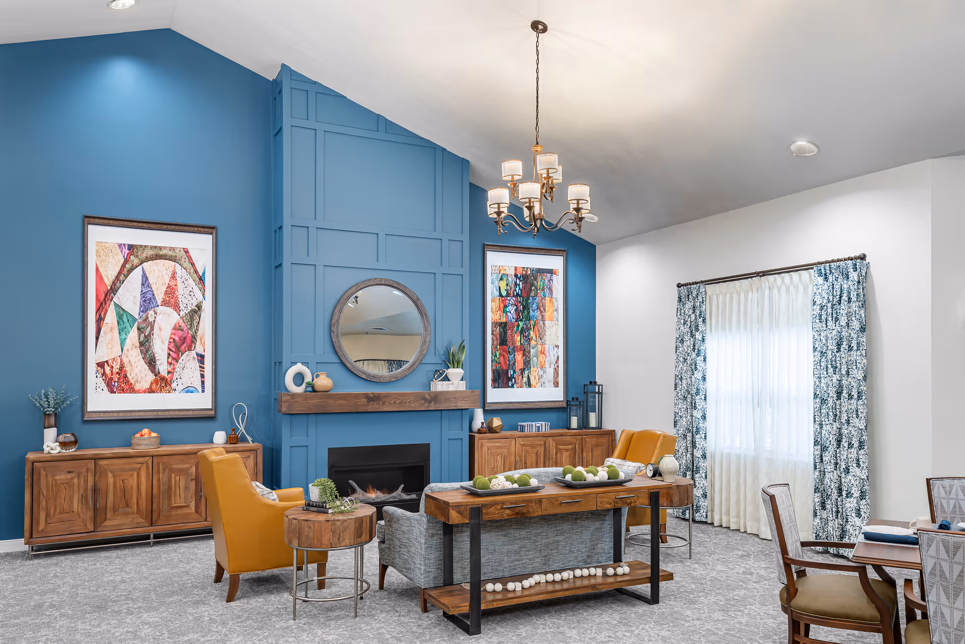 Well-lit communal living room with a blue paneled accent wall and fireplace, seating, artwork, and a dining area.