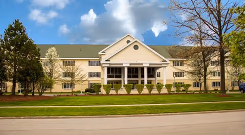 Exterior view of Colonial Villa of Midland: a beige building with a white entrance and shrubs.