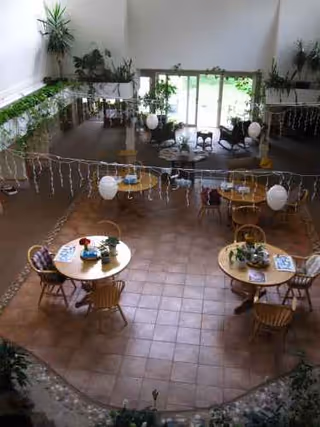 Interior atrium with round dining tables, chairs, plants, and festive string lights.