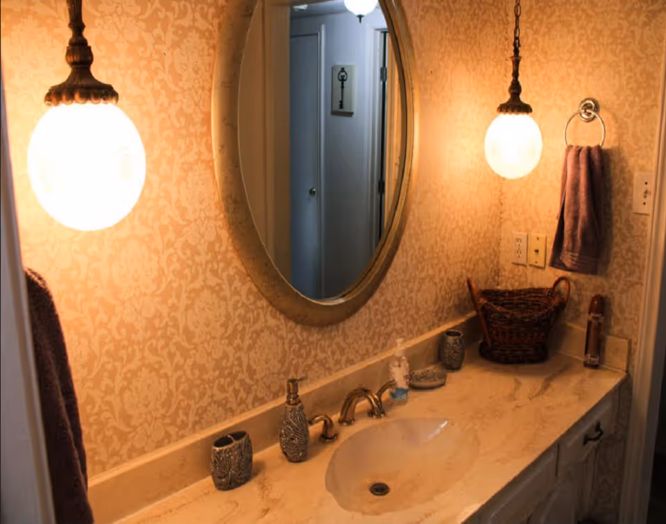Bathroom vanity with an oval mirror, marble countertop and sink, two hanging globe lights, a towel, and decorative accessories.