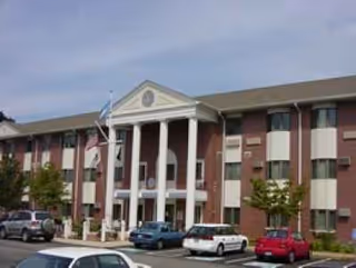 Brick apartment building with white columns and a centered entrance facing a parking lot.