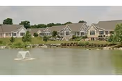 Row of single-story cottage-style buildings along a pond with a central fountain.