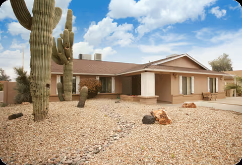 Single-story beige care home with desert landscaping and large cacti in the front yard.