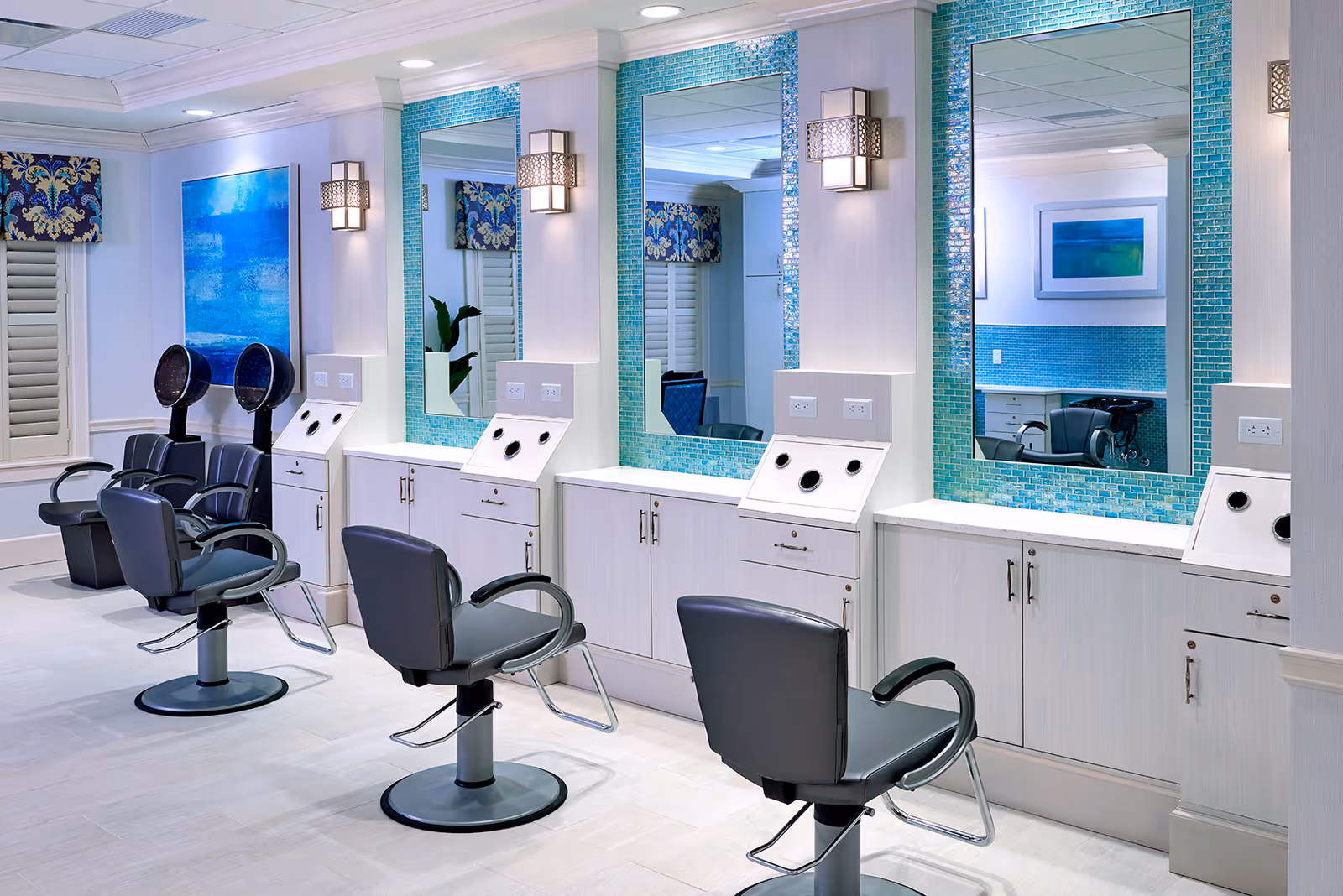 Bright salon area with styling chairs, large mirrors framed in turquoise mosaic tiles, and hooded hair dryers.