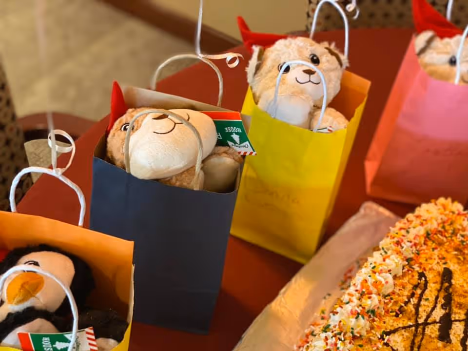 Gift bags with stuffed animals arranged on a table next to a decorated sheet cake.