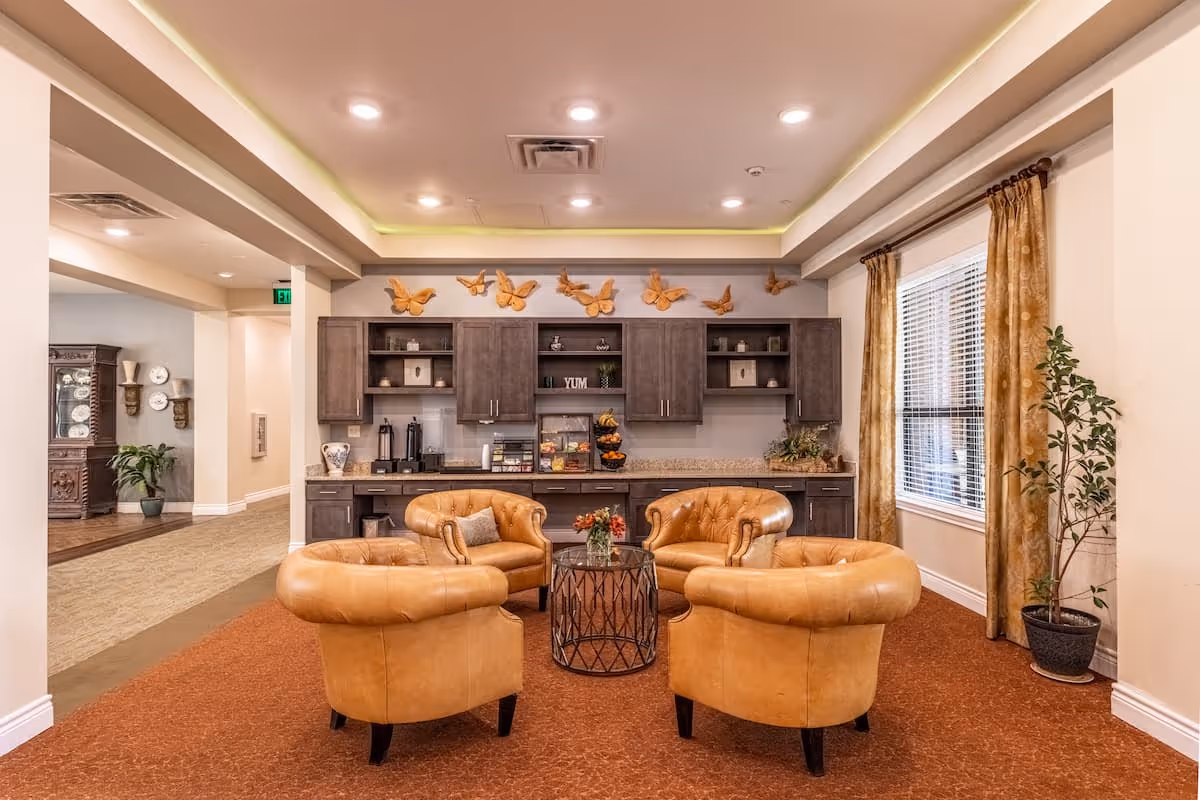 A cozy interior lounge with four tan leather armchairs arranged around a round table in front of built-in cabinets and a window.