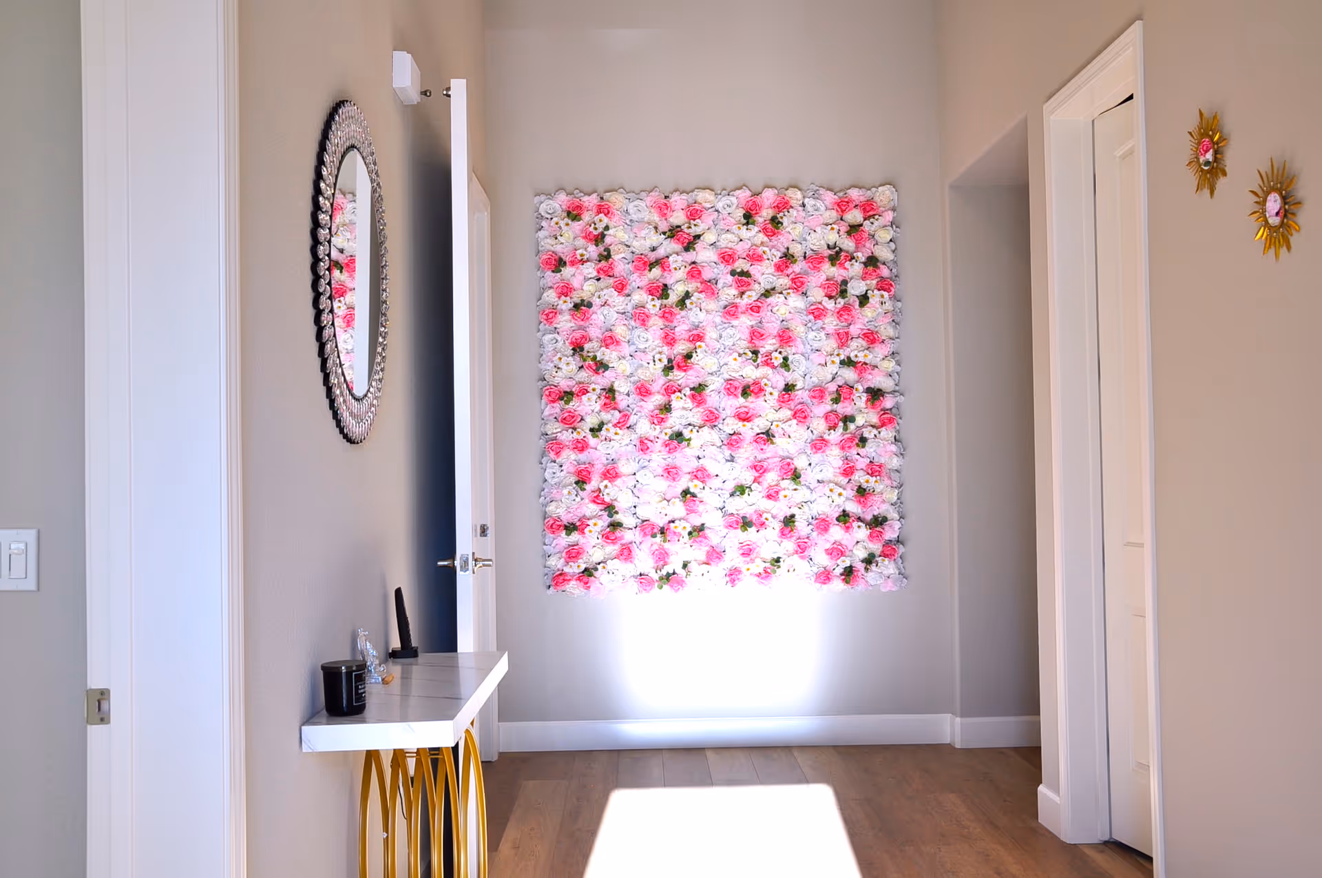 Hallway interior featuring a large square panel of pink and white flowers on the wall, a small console table with gold legs and a round mirror.