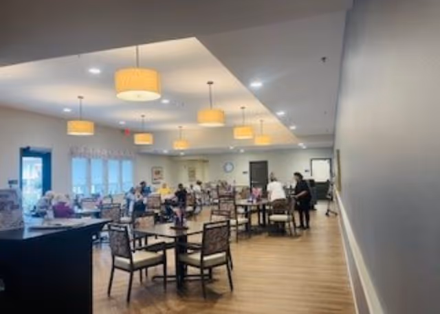 Large senior living dining room with multiple round tables and chairs and residents seated under pendant lights.