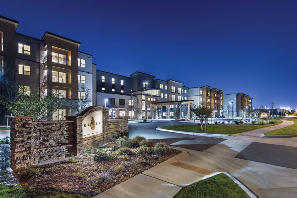 Nighttime exterior view of Revel Province senior living building with illuminated entrances and landscaping.