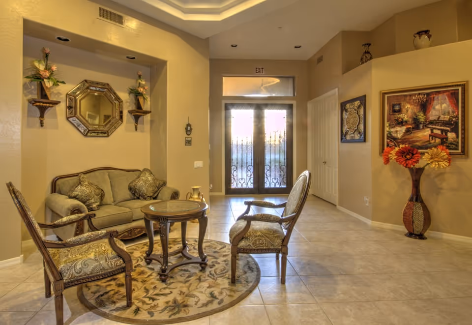 A warmly decorated sitting area with a sofa, two armchairs and a round table on a patterned rug in front of decorative double glass entry doors.