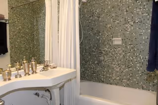 Bathroom with a white sink and faucet, a bathtub with a shower curtain, and green mosaic-tiled walls.