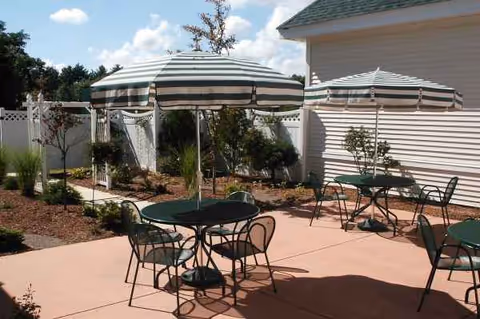 Outdoor patio with striped umbrellas, round tables, and metal chairs beside a light building.