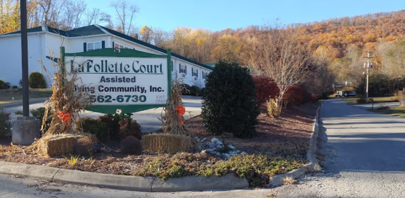 Outdoor view of La Follette Court Assisted Living Community sign with a building and trees in the background during autumn.