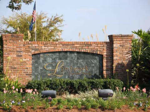 Brick entrance sign for Landmark of Baton Rouge with landscaping and an American flag.