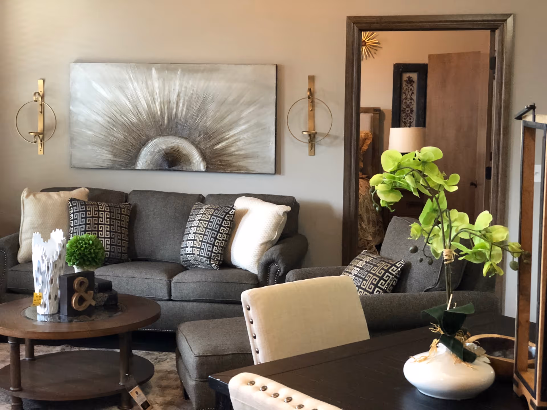 Cozy living room with a gray sofa and patterned pillows, a round coffee table, and a green potted plant on a nearby table in the foreground.
