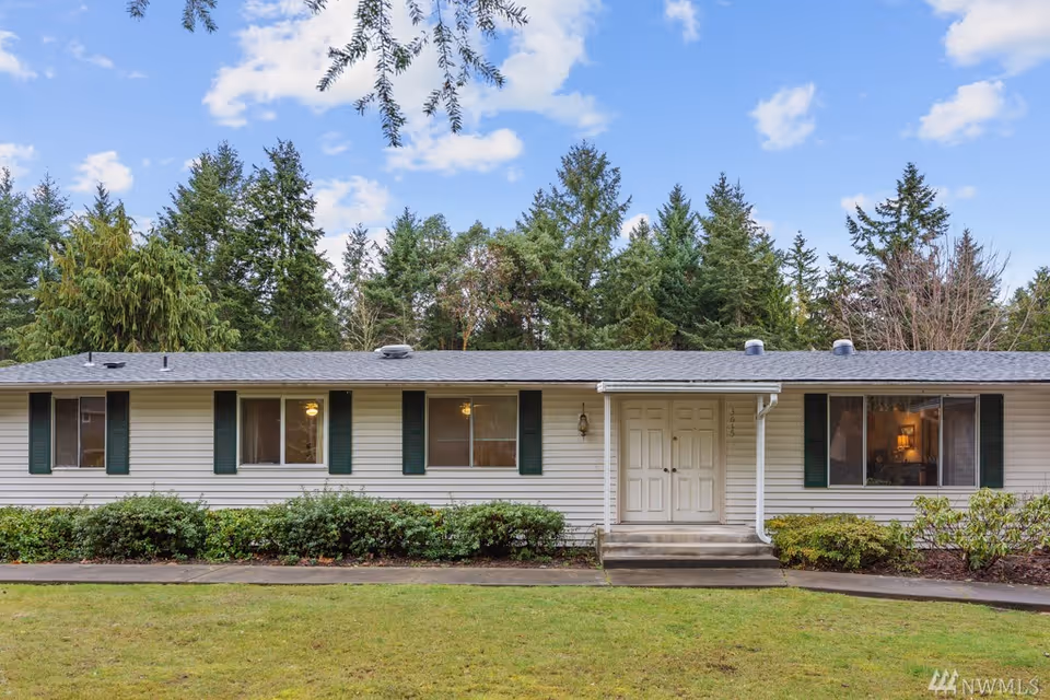 Single-story white ranch-style building with green shutters, a double front door, lawn, and trees in the background.