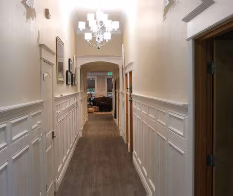 Long, well-lit hallway in a Mercy Family Home facility with paneled walls, doors, and a chandelier.