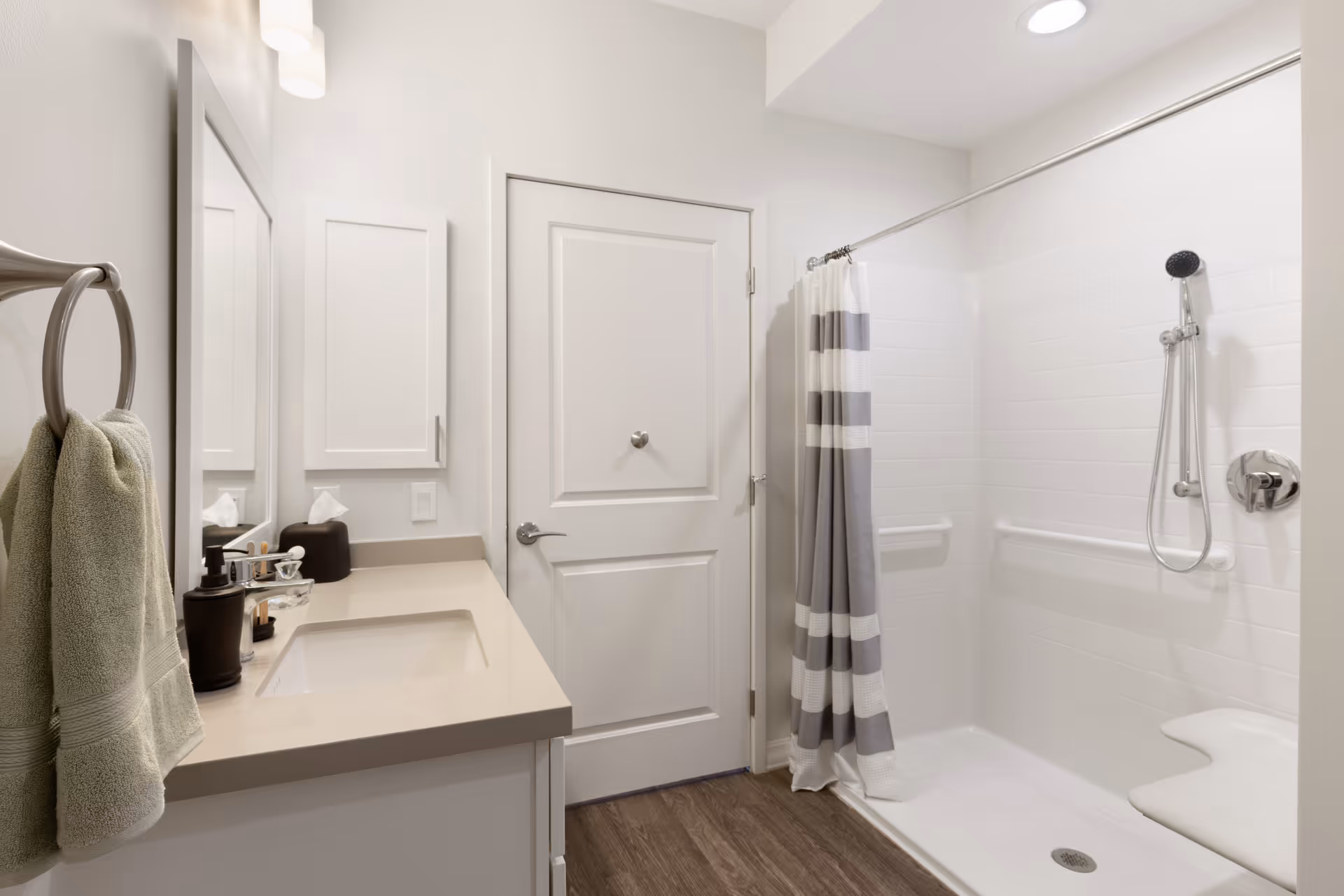 Bright accessible bathroom with a vanity and mirror on the left and a walk-in shower with grab bars and a striped curtain on the right.