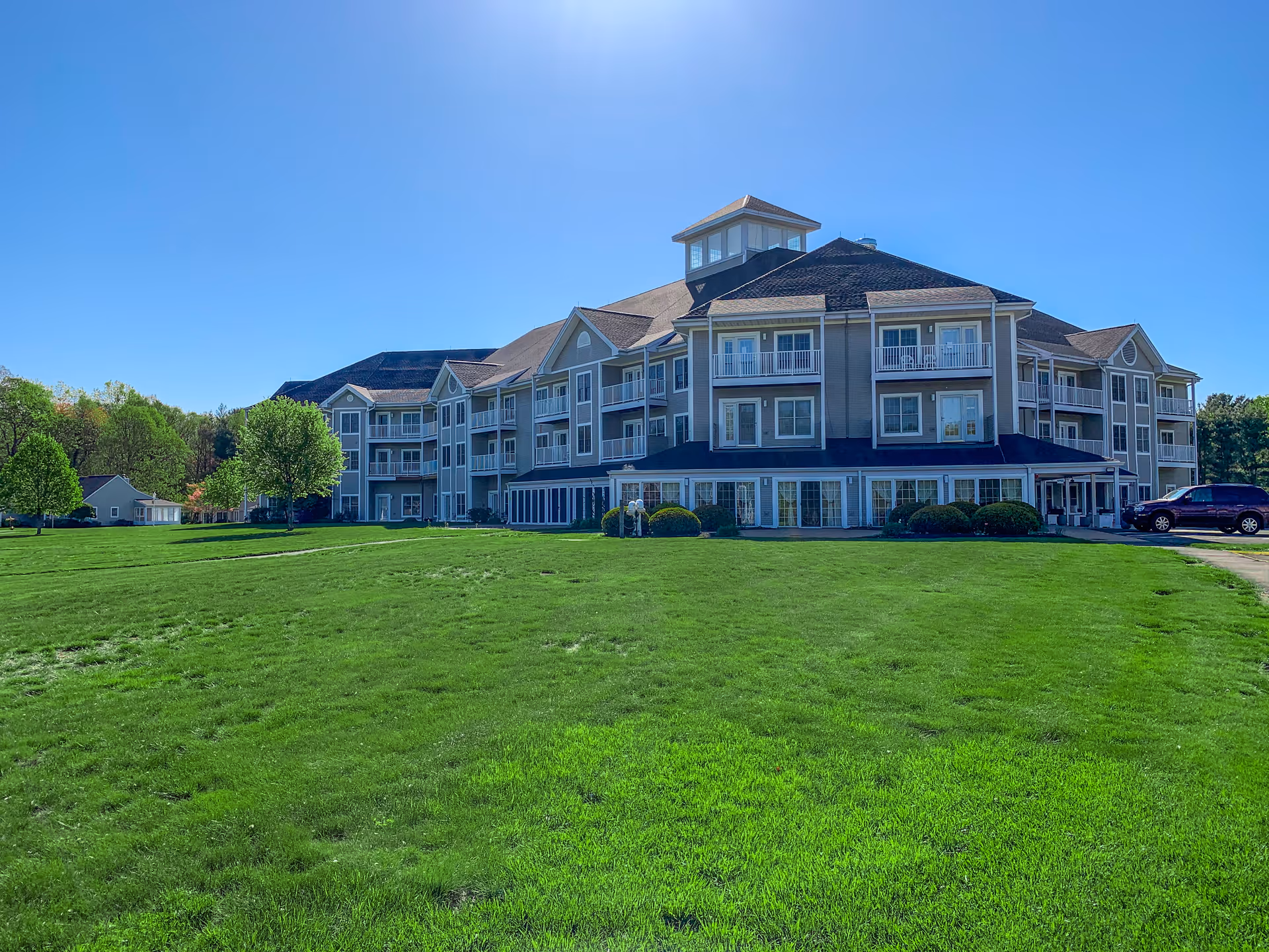 Large three-story residential building with balconies overlooking a wide green lawn under a clear blue sky.