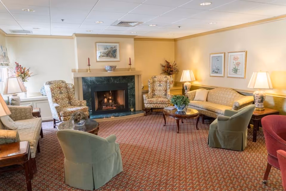 Comfortable common lounge with a lit fireplace, upholstered chairs and sofas, coffee tables and lamps.