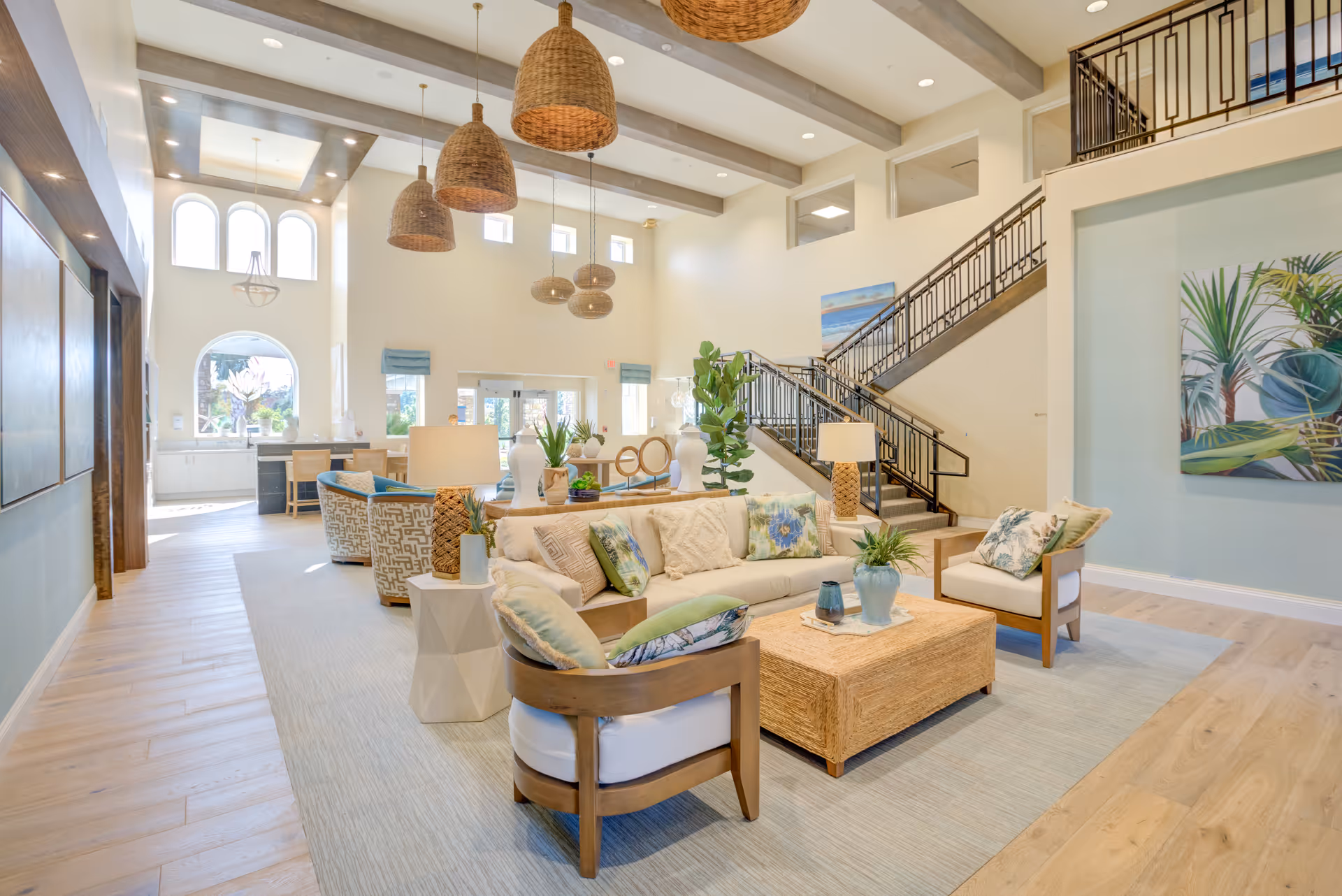 Bright, coastal-style common lounge with sofas, armchairs, woven pendant lights, a coffee table, and a staircase.