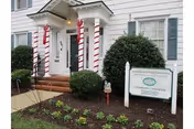 Front entrance of a white townhome building with candy-cane striped columns, trimmed bushes, and a sign in the landscaped yard.