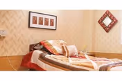 Small bedroom with a single bed covered in a patterned quilt, decorative pillows, framed artwork and a wall mirror on wallpapered walls.
