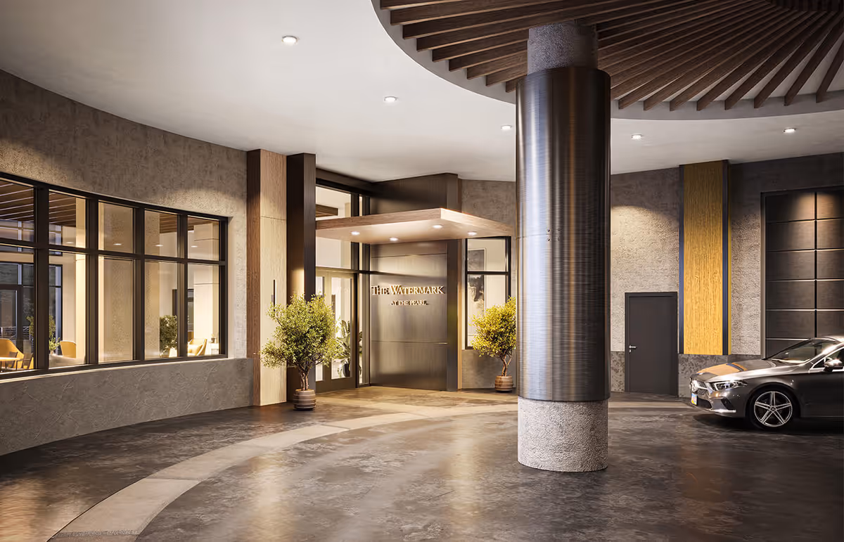 Covered entrance area of The Watermark at the Pearl facility with a modern design, featuring large windows, two potted plants flanking the entrance door, a large cylindrical column, and a parked silver car on the right side.