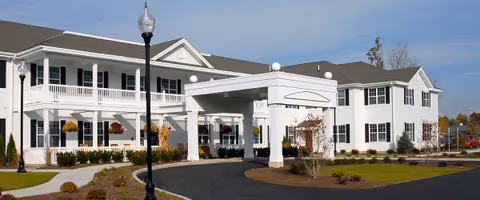 White two-story senior living facility with a porte-cochere and landscaped entrance.
