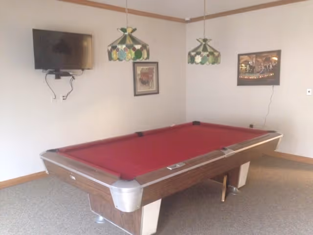 Room featuring a red-felt pool table with stained-glass pendant lights, a wall-mounted TV and framed pictures.