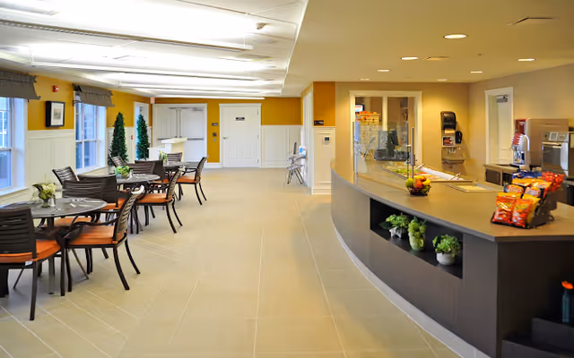 Bright communal dining and snack area with multiple tables and chairs and a curved service counter.