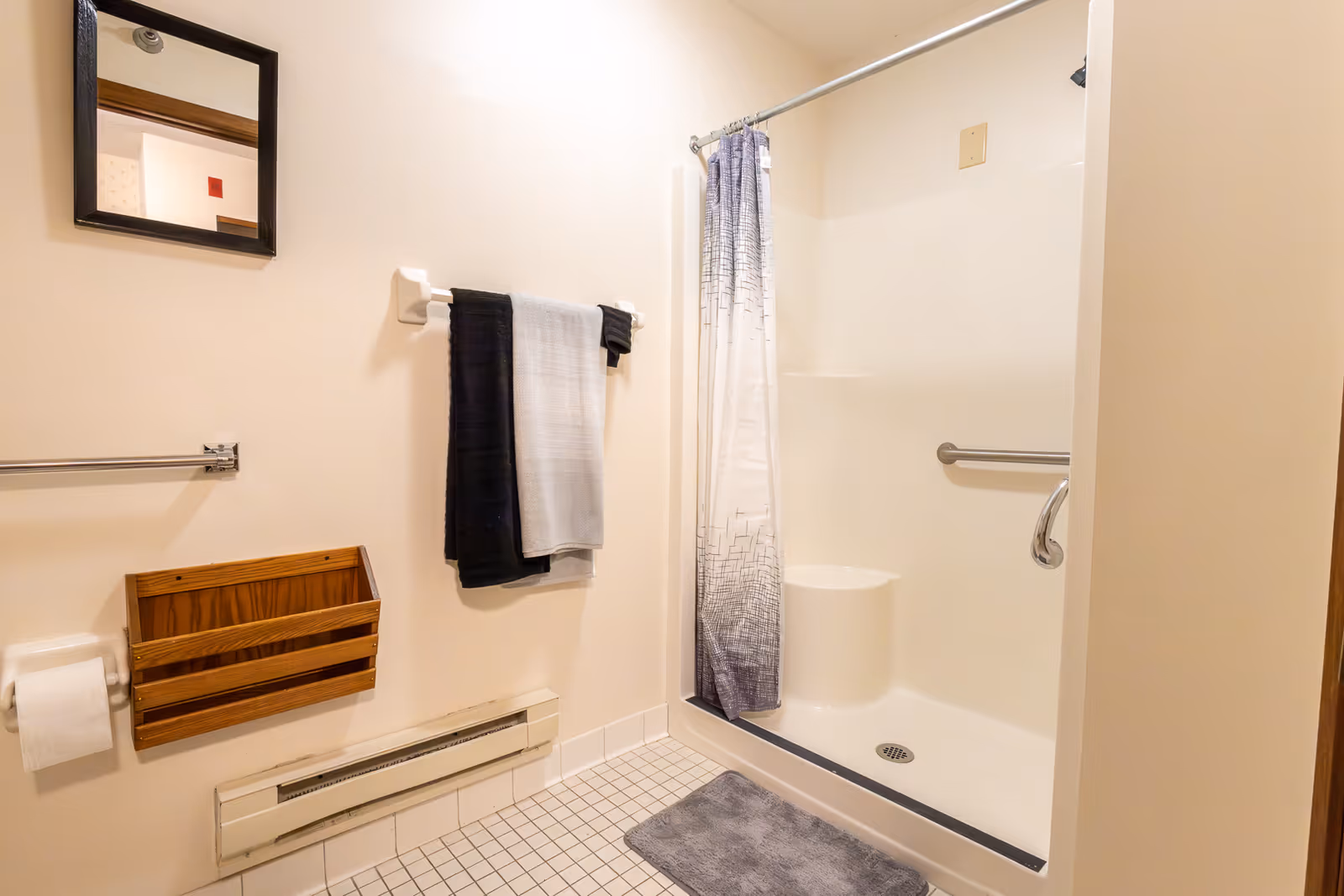 Accessible bathroom with a walk-in shower and grab bar, towel rack, small mirror, and tiled floor.