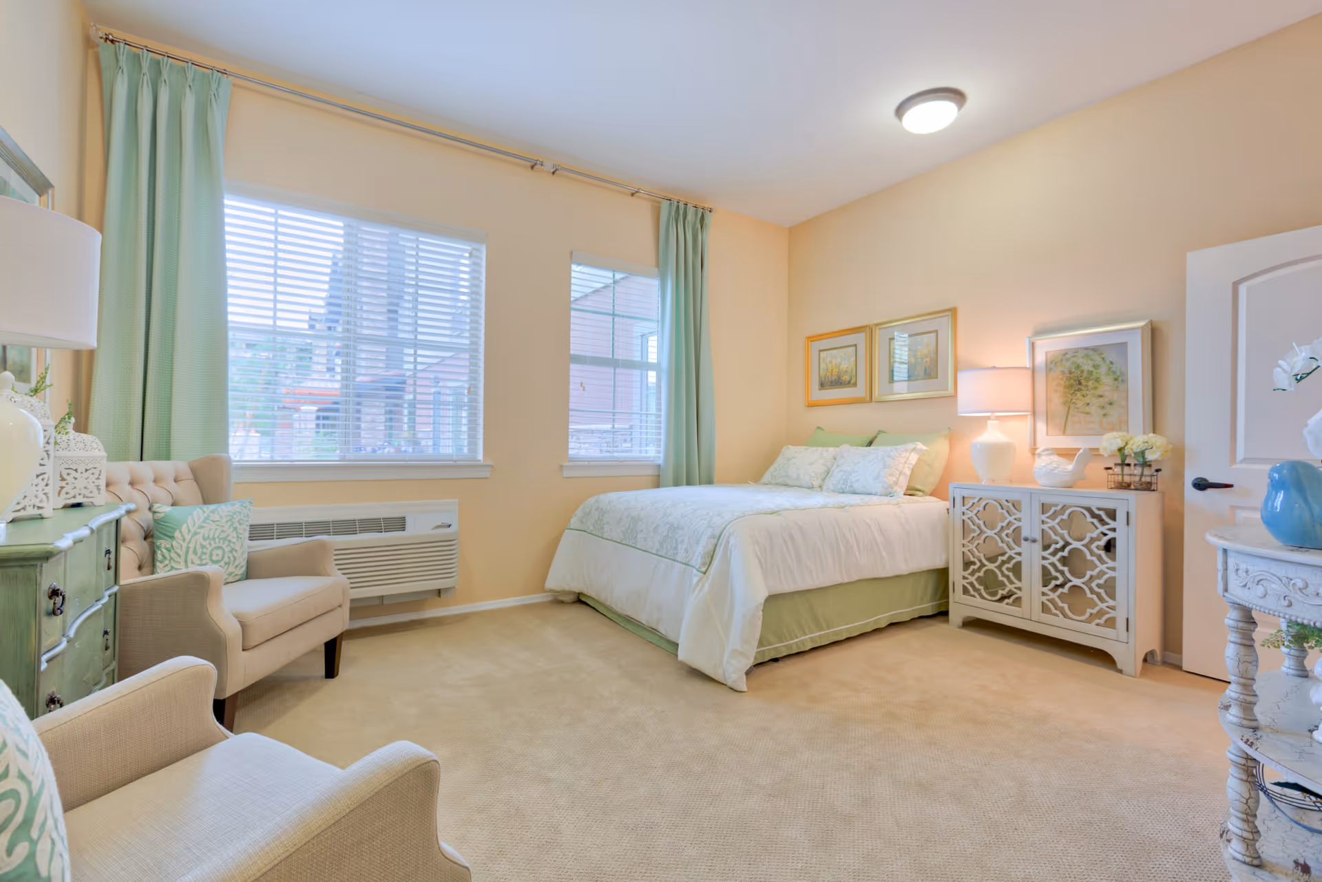 Sunlit bedroom with a bed, bedside cabinet, two armchairs, and mint-green accents.