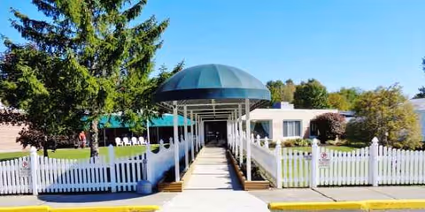 Covered walkway leads to Betsy Ross Nursing Facility entrance with white picket fencing.