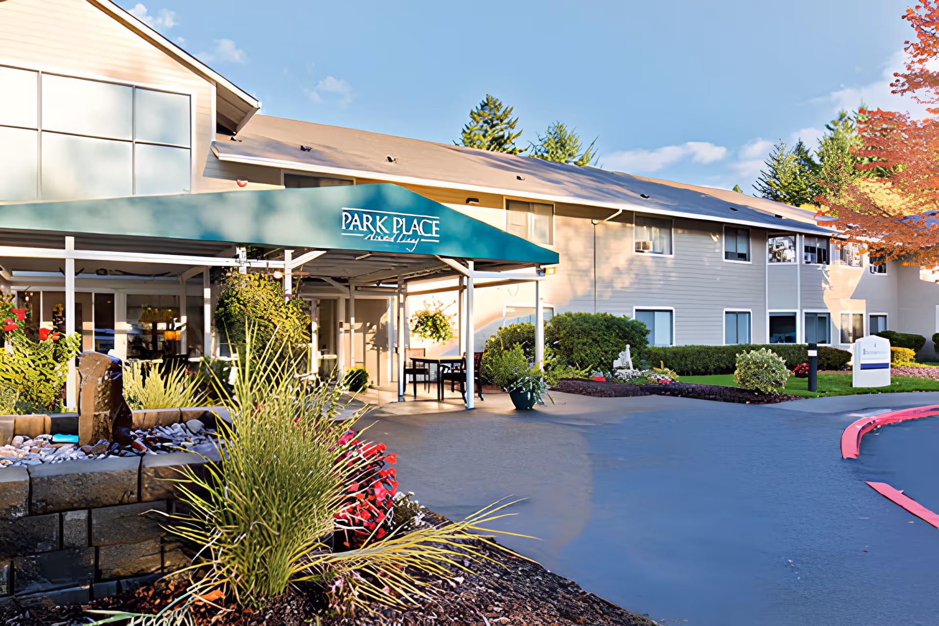 Front entrance of the Park Place senior living facility with a green canopy over the driveway, landscaped planters, and the two-story building.