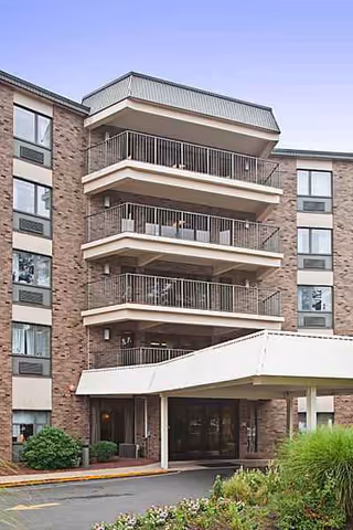 Brick senior living building with balconies and a covered entrance.
